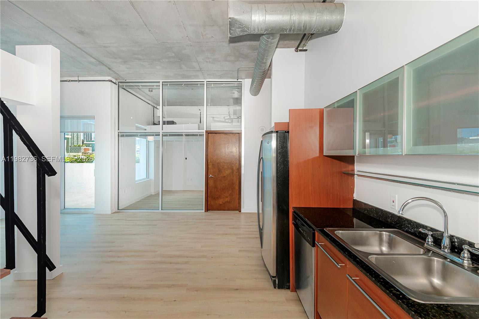 A kitchen with stainless steel appliances and wood cabinets opens to a room with glass walls — 10 SW South River Dr # 607, Miami FL 33130, MIAMI, FL
