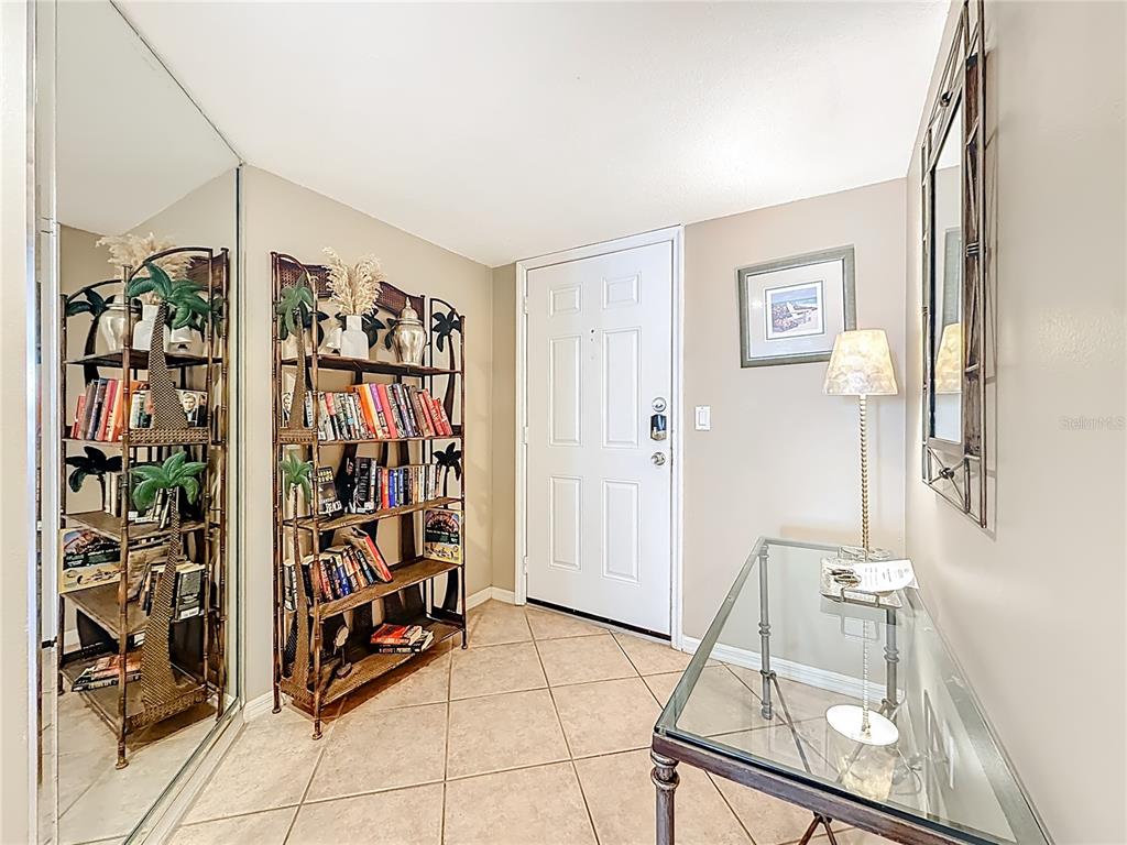 An entryway features tile flooring, a bookshelf, a glass console table, and a mirrored closet — 18400 GULF BOULEVARD UNIT 1312, INDIAN SHORES, FL