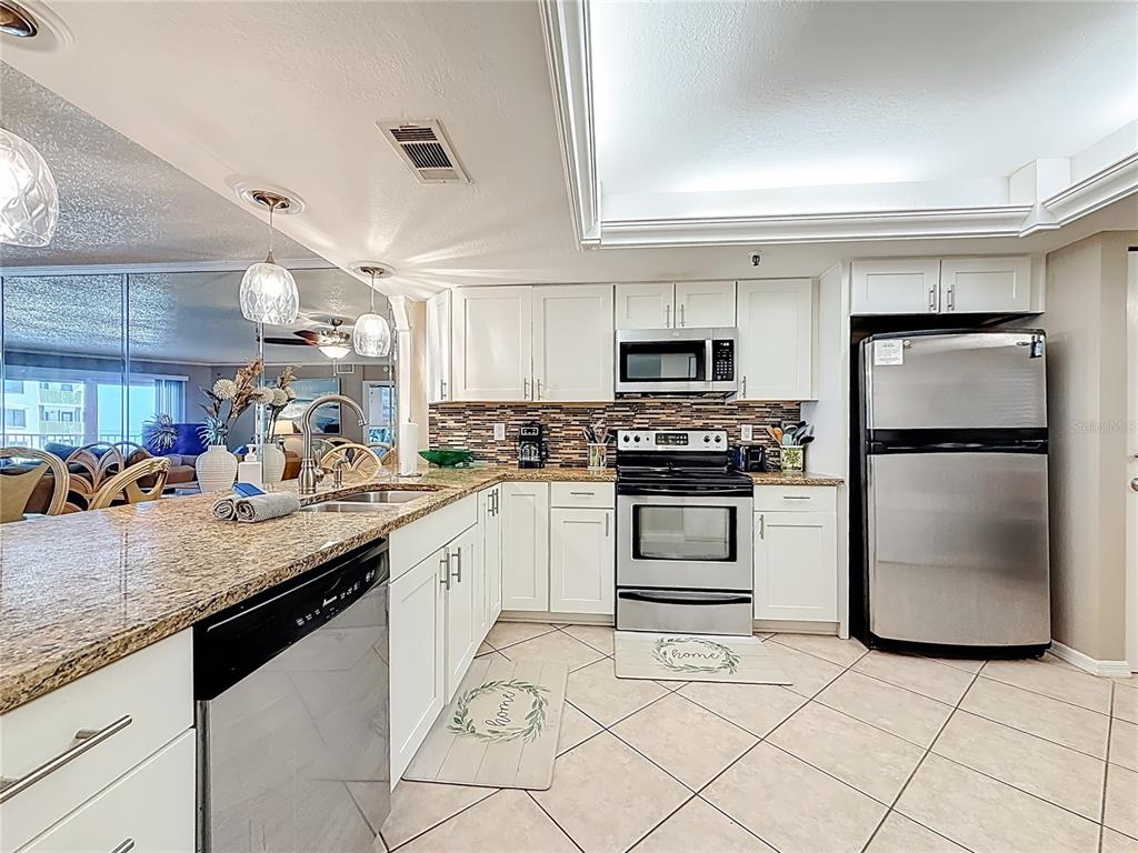 A kitchen features white cabinets, granite countertops, stainless steel appliances, and diagonal floor tiles — 18400 GULF BOULEVARD UNIT 1312, INDIAN SHORES, FL