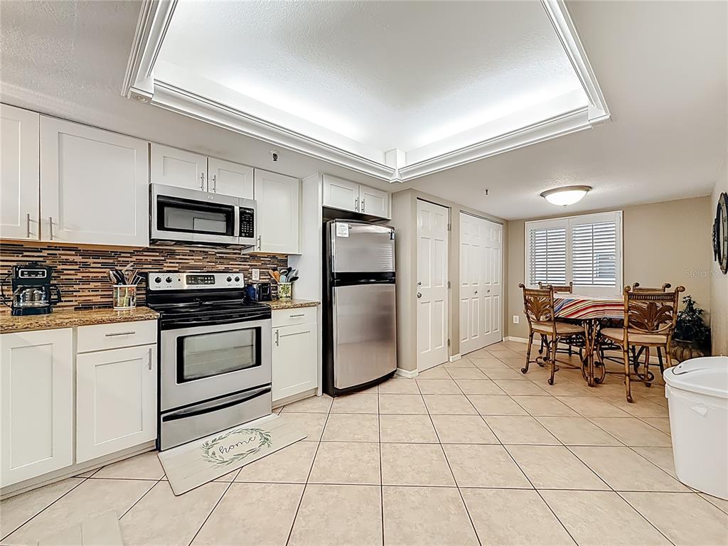 A kitchen with white cabinets, stainless steel appliances, a tiled backsplash, and a dining area — 18400 GULF BOULEVARD UNIT 1312, INDIAN SHORES, FL