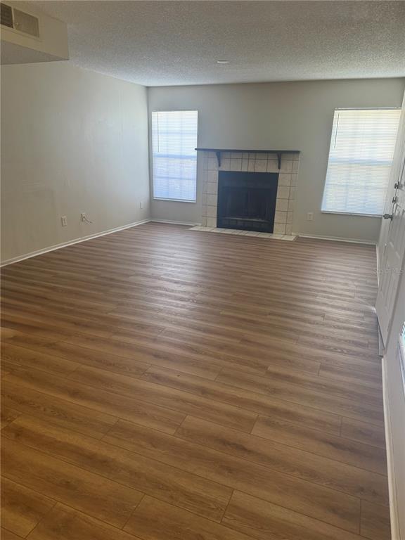 An empty living room features wood-look flooring, a fireplace with a tiled surround, and windows — 3028 BONAVENTURE CIRCLE UNIT 103, PALM HARBOR, FL