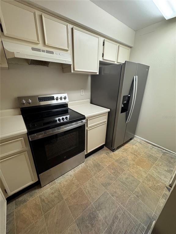 A kitchen features off-white cabinets, a stainless steel stove, and a gray side-by-side refrigerator — 3028 BONAVENTURE CIRCLE UNIT 103, PALM HARBOR, FL