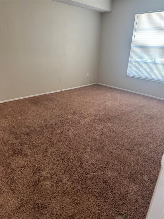 An empty bedroom with beige walls, brown carpet, and a window with white blinds — 3028 BONAVENTURE CIRCLE UNIT 103, PALM HARBOR, FL