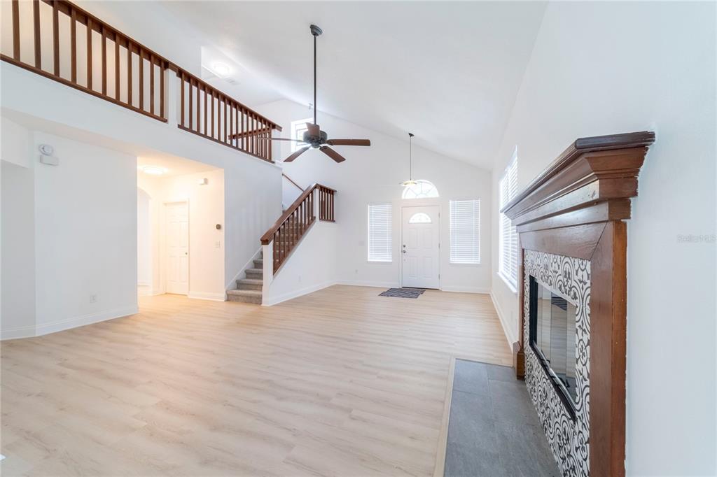 A living room features a fireplace, vaulted ceilings, a staircase, and light wood-look flooring — 499 JULIAN LANE, MAITLAND, FL