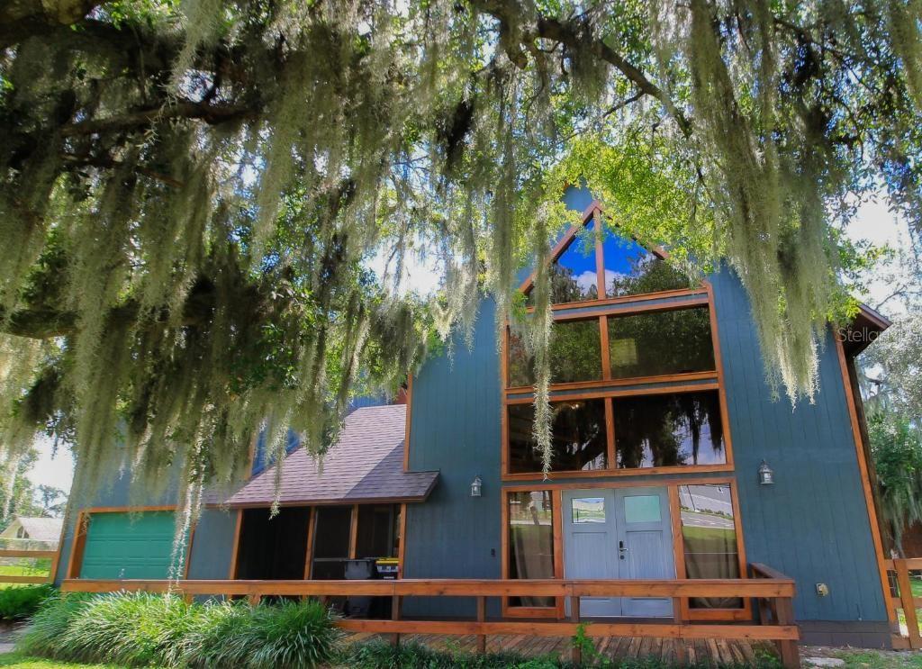 A blue A-frame house with large windows and a wooden deck under mossy trees — 4840 OLD LUCERNE PARK RD, WINTER HAVEN, FL
