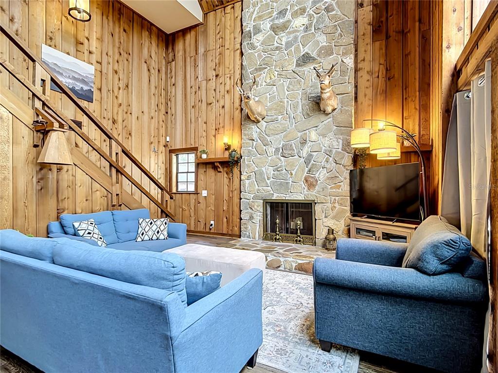 A living room features wood-paneled walls, a stone fireplace with taxidermy, and blue furniture — 4840 OLD LUCERNE PARK RD, WINTER HAVEN, FL