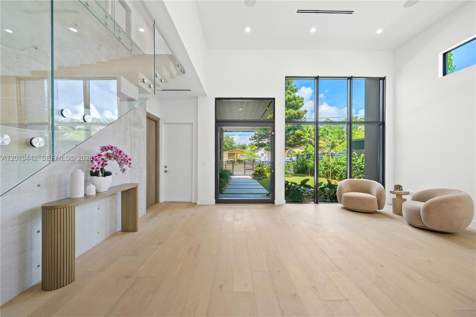 A modern entryway features light wood floors, a glass staircase, and floor-to-ceiling windows — 280 NW 47th St, Miami FL 33127, MIAMI, FL