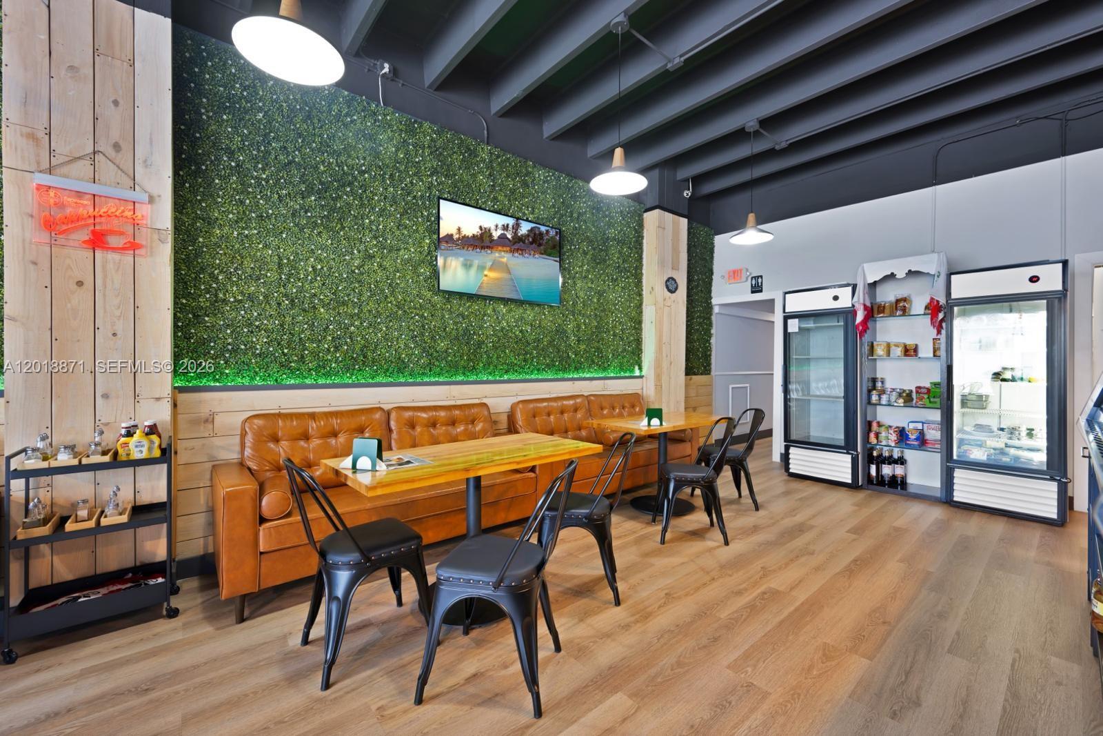 A cafe interior features a green wall, leather banquette seating, wooden tables, and two refrigerators — 422 S Dixie Hwy, Hollywood FL 33020, HOLLYWOOD, FL