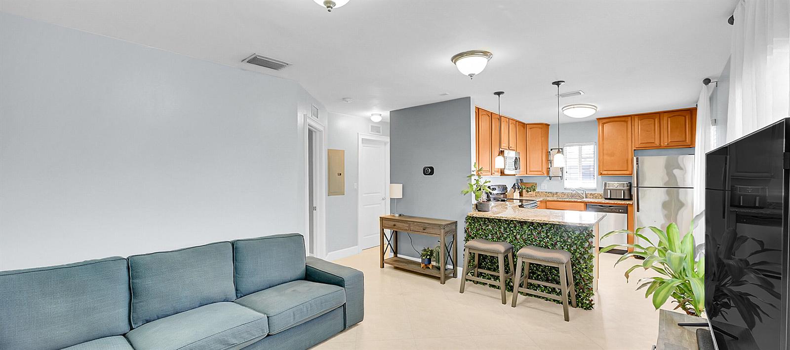 A living room with a blue sofa opens to a kitchen featuring wood cabinets — 410 SW 15th Street # 206, Pompano Beach FL 33060, POMPANO BEACH, FL