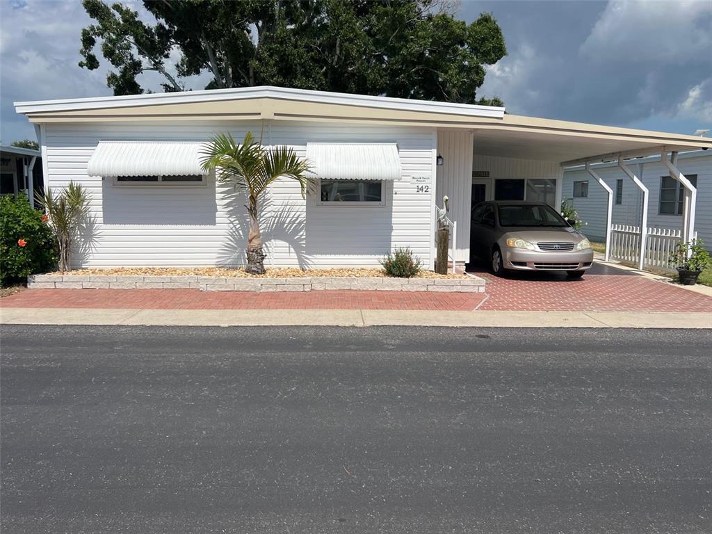 A single-story mobile home features white horizontal siding, a carport, and a paved driveway — 142 FERN PALM STREET, LARGO, FL