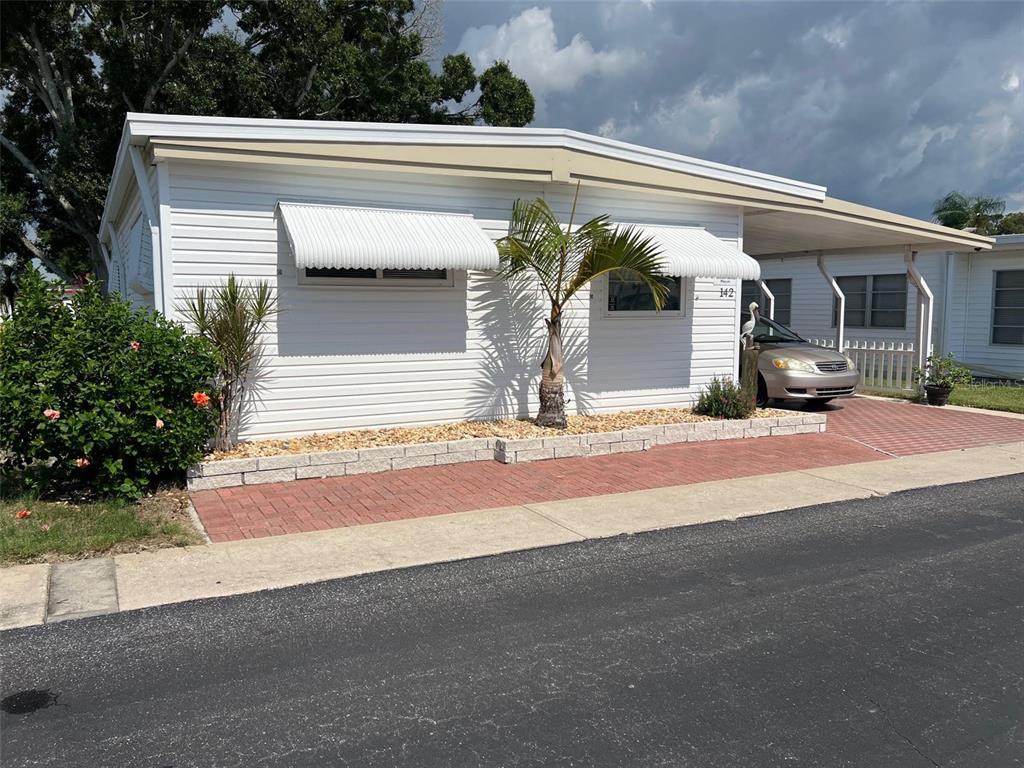 A white mobile home with a carport, brick driveway, and small palm tree in front — 142 FERN PALM STREET, LARGO, FL