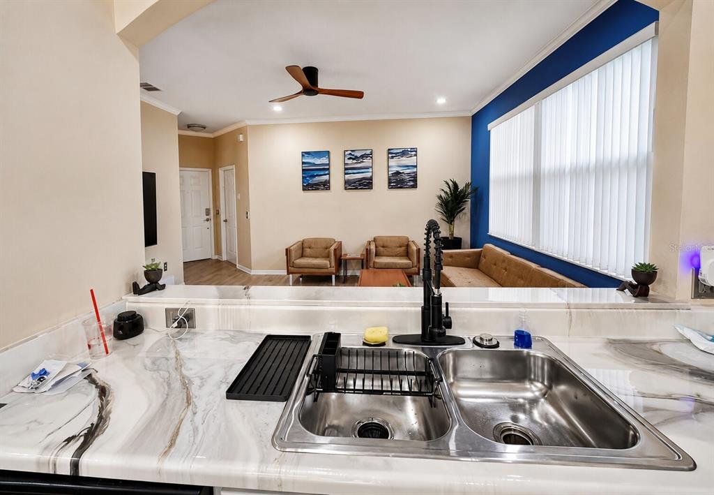 A kitchen sink with a marble countertop overlooks a living room with tan furniture — 15728 GREEN COVE BOULEVARD, CLERMONT, FL
