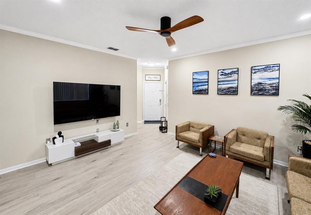 A living room features light wood-look flooring, a wall-mounted television, and two tan armchairs — 15728 GREEN COVE BOULEVARD, CLERMONT, FL