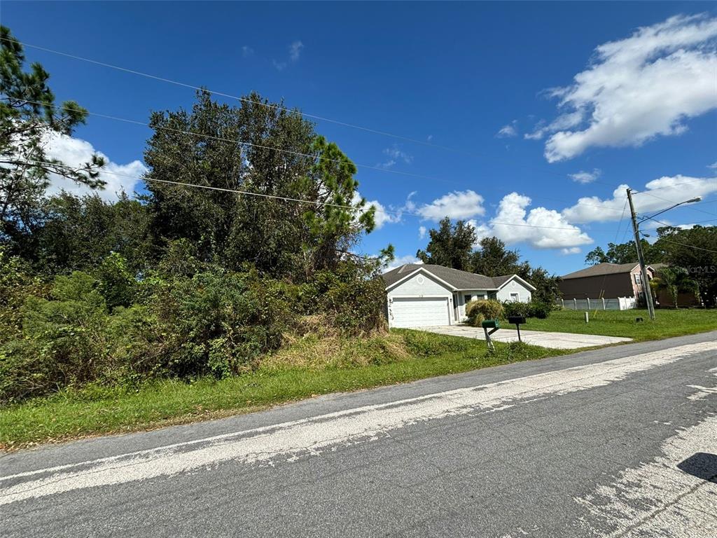 A single-story house with a white garage sits next to a large, overgrown wooded lot — 310 CARDIFF DRIVE, POINCIANA, FL