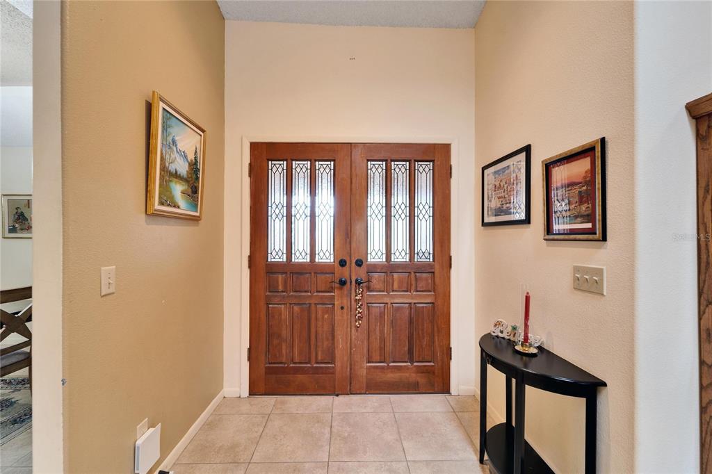 A tiled entryway features double wooden front doors with glass panels and decorative wall art — 2913 ASTON AVENUE, PLANT CITY, FL