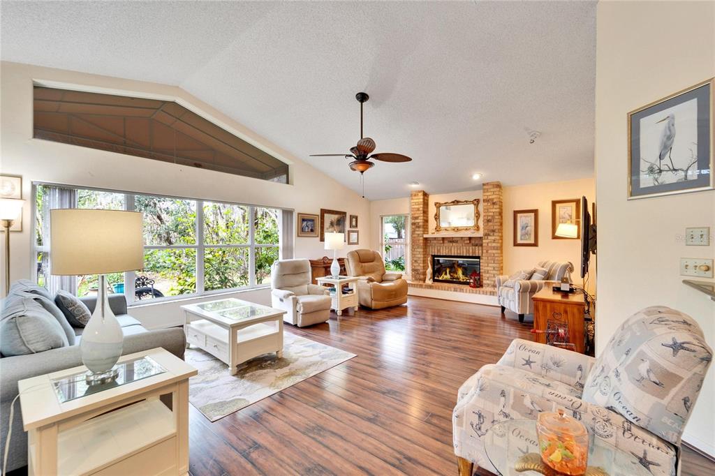 A living room features a brick fireplace, hardwood floors, and large windows with vaulted ceilings — 2913 ASTON AVENUE, PLANT CITY, FL
