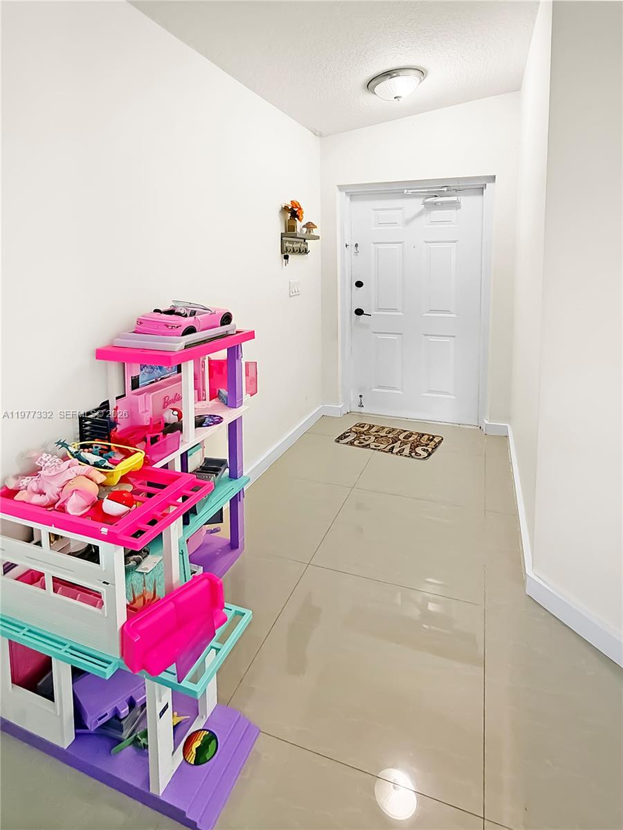 A brightly lit entryway features white walls, tile flooring, and a large Barbie dollhouse — 945 NE 34th Ave # 204, Homestead FL 33033, HOMESTEAD, FL