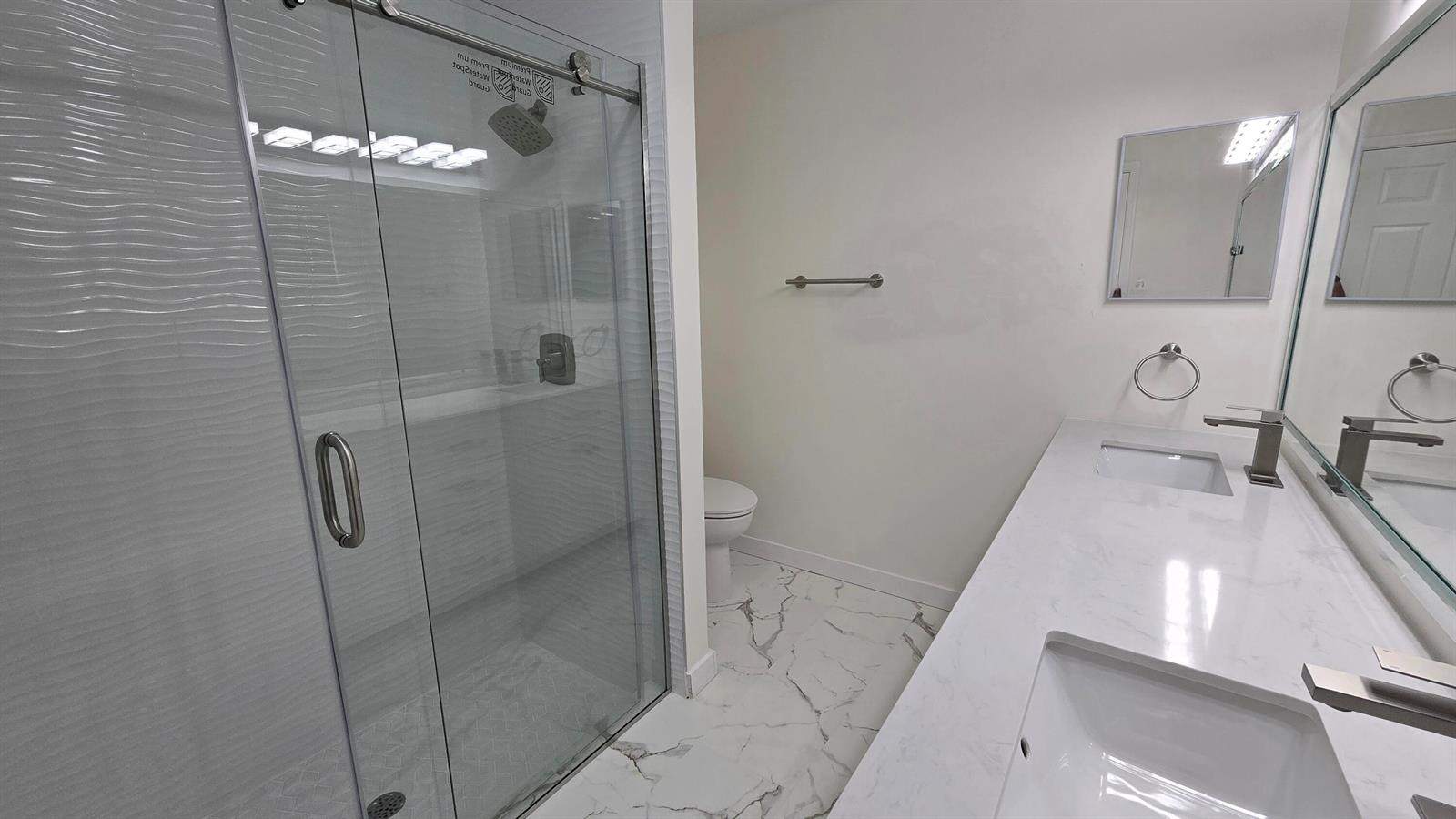 A modern bathroom features a glass-enclosed shower, a double vanity with marble countertops, and tiled flooring — 5622 Royal Lake Circle, Boynton Beach FL 33437, BOYNTON BEACH, FL