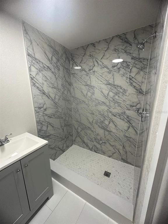 A bathroom featuring a gray vanity and a walk-in shower with marble-patterned tile walls — 1150 PIPPIN STREET, JACKSONVILLE, FL