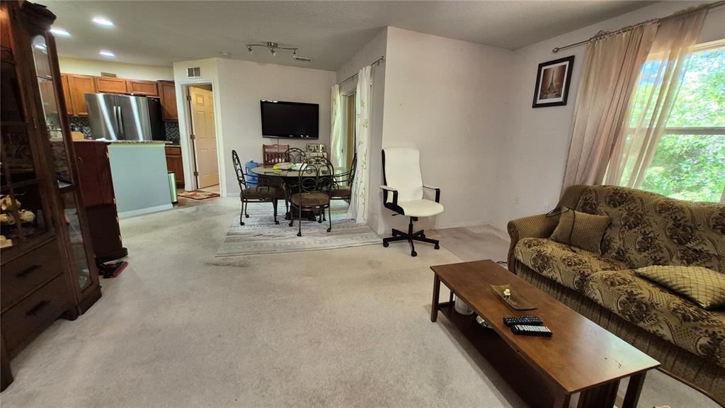 A living room with beige carpet, a patterned sofa, a coffee table, and a dining area — 4600 E MOODY BOULEVARD UNIT 8M, BUNNELL, FL