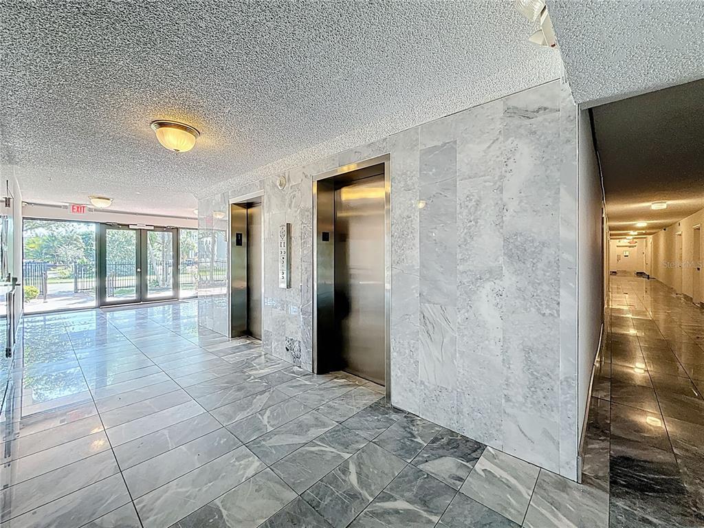 An elevator lobby features marble walls, tiled floors, and a view of an outdoor area — 12500 NE 15TH AVENUE UNIT 105, NORTH MIAMI, FL