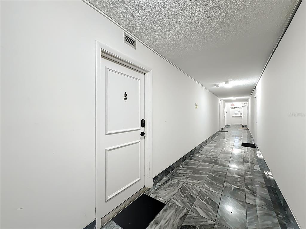 A long hallway features white walls, a textured ceiling, and gray marble-patterned tile flooring — 12500 NE 15TH AVENUE UNIT 105, NORTH MIAMI, FL