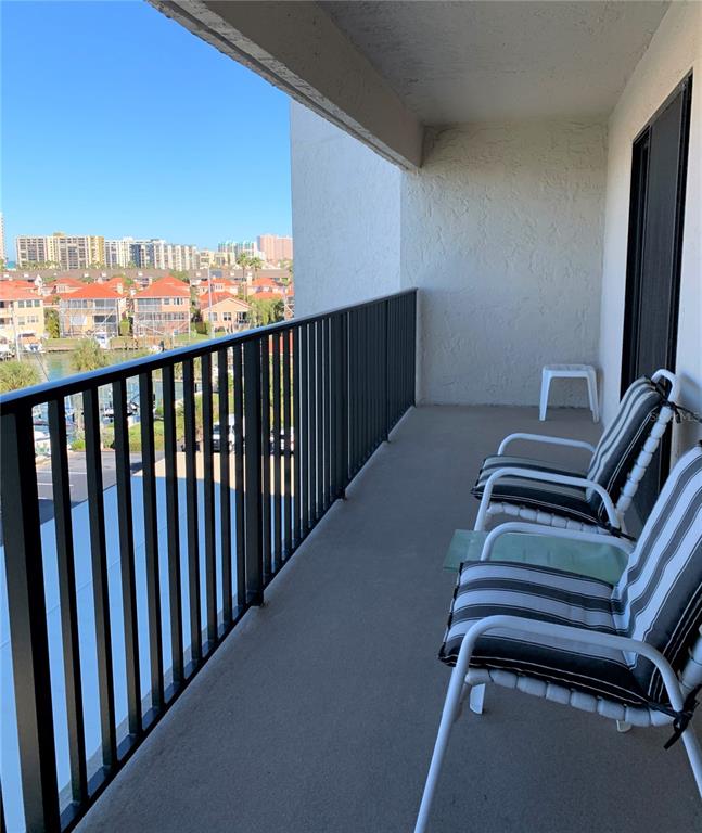 A balcony with metal railings overlooks a waterfront neighborhood with two striped chairs — 240 SAND KEY ESTATES DRIVE UNIT 257, CLEARWATER, FL