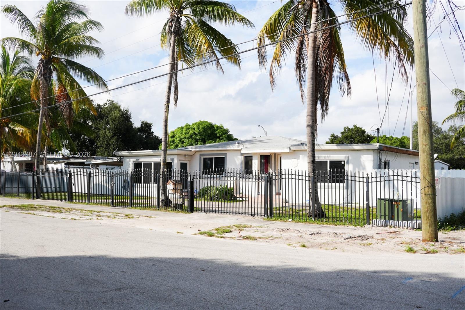 A single-story white house with a black metal fence sits behind palm trees — 2955 NW 102nd St, Miami FL 33147, MIAMI, FL