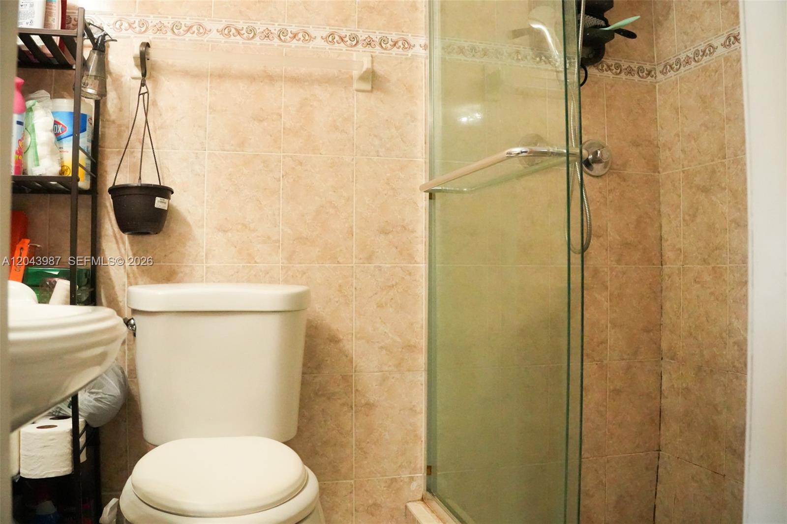 A bathroom features a toilet, a glass-enclosed shower, and beige tiled walls — 2955 NW 102nd St, Miami FL 33147, MIAMI, FL