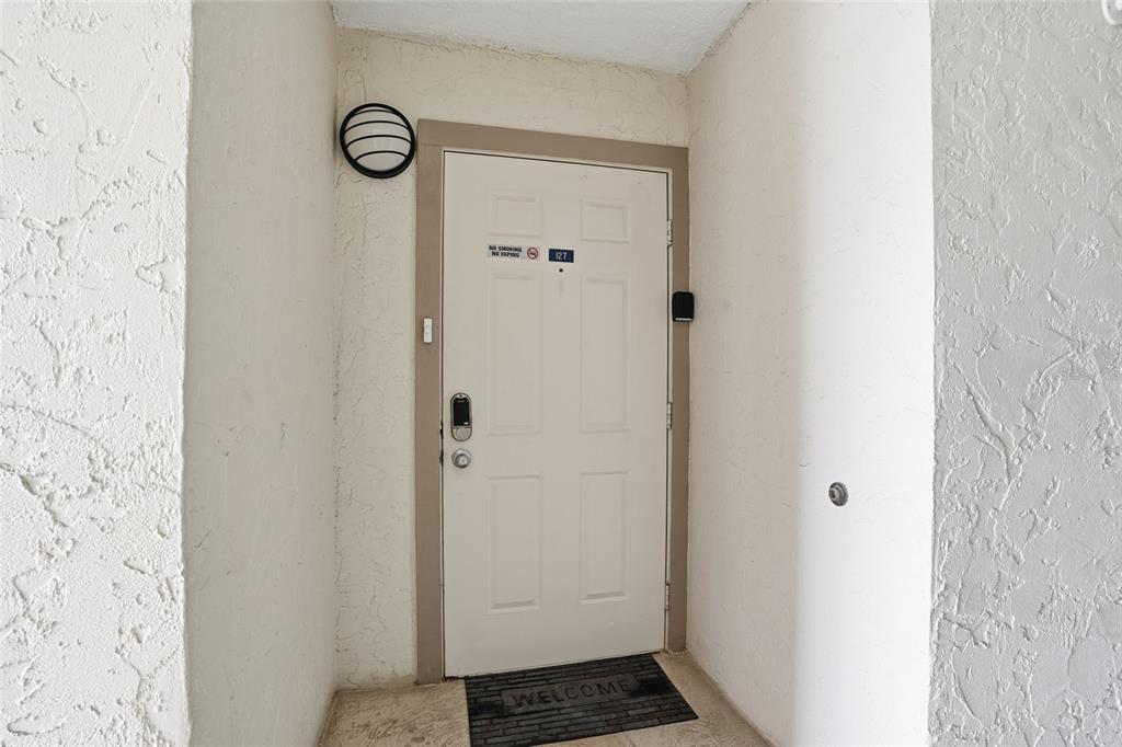 A white front door with a smart lock and a welcome mat in a recessed entryway — 3170 MATECUMBE KEY ROAD UNIT 127, PUNTA GORDA, FL