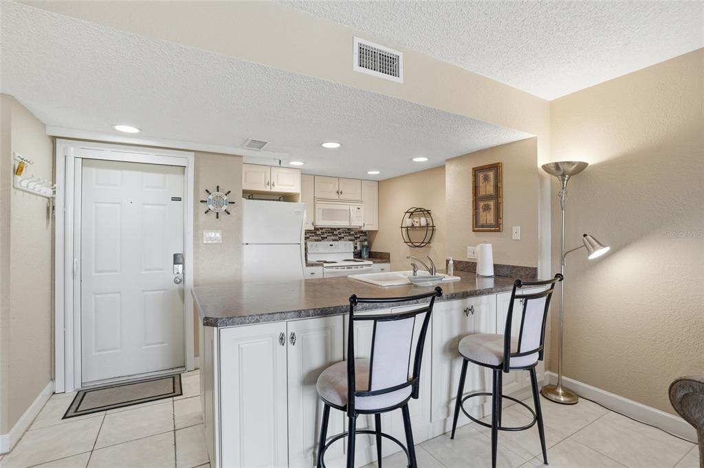 A kitchen features white cabinets, a dark countertop, two bar stools, and a white door — 3170 MATECUMBE KEY ROAD UNIT 127, PUNTA GORDA, FL