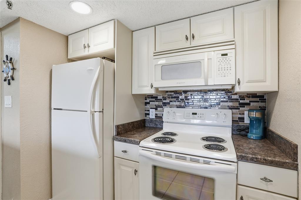A kitchen features white cabinets, white appliances, dark countertops, and a multi-colored glass tile backsplash — 3170 MATECUMBE KEY ROAD UNIT 127, PUNTA GORDA, FL