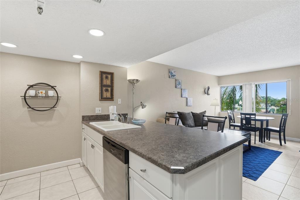 A kitchen with white cabinets and dark countertops overlooks a living and dining area — 3170 MATECUMBE KEY ROAD UNIT 127, PUNTA GORDA, FL
