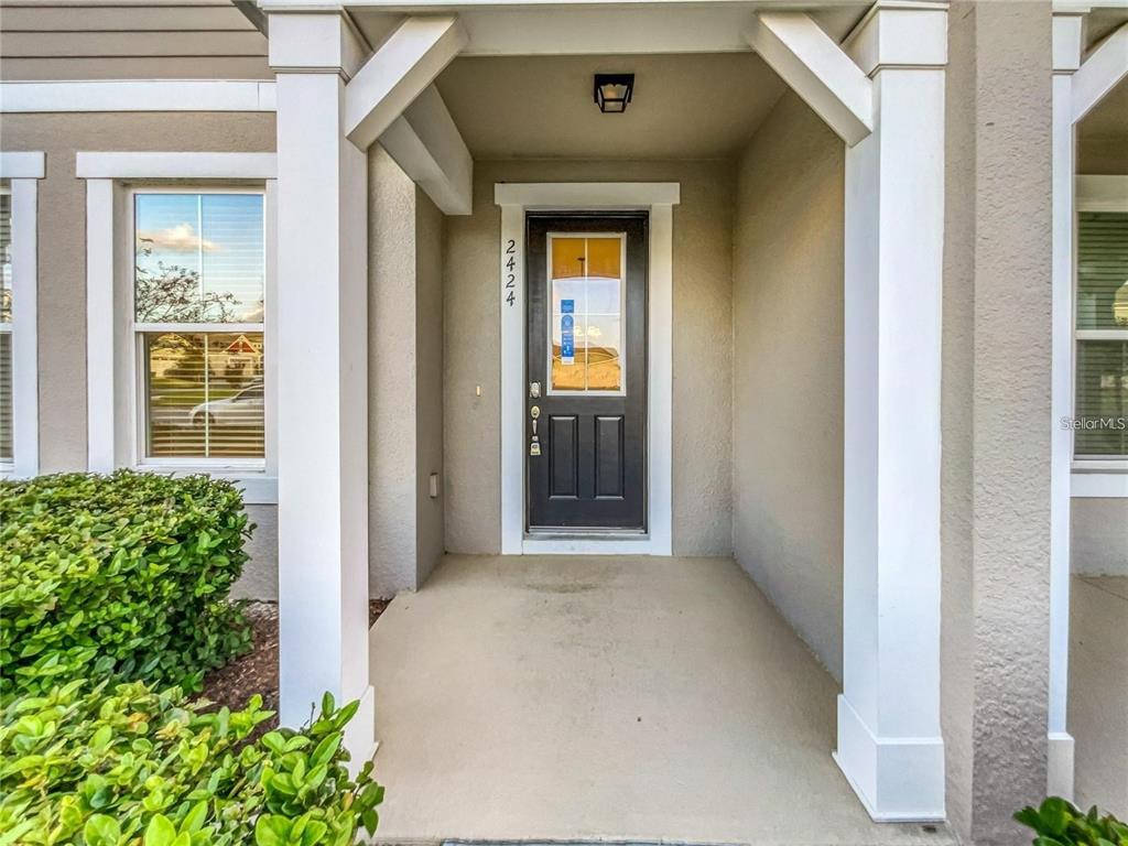 A covered front porch with a dark door and white columns leads to the entrance — 2424 BLOWING BREEZE AVENUE, KISSIMMEE, FL