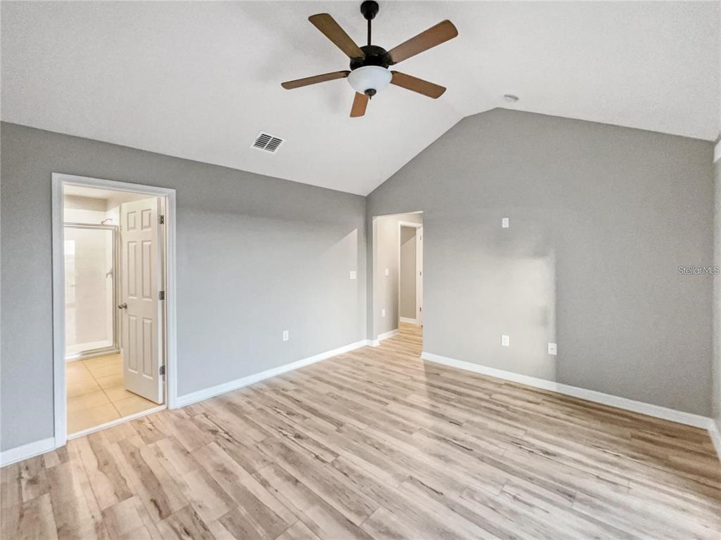 A bedroom with light gray walls, wood-look flooring, a vaulted ceiling, and a ceiling fan — 2424 BLOWING BREEZE AVENUE, KISSIMMEE, FL
