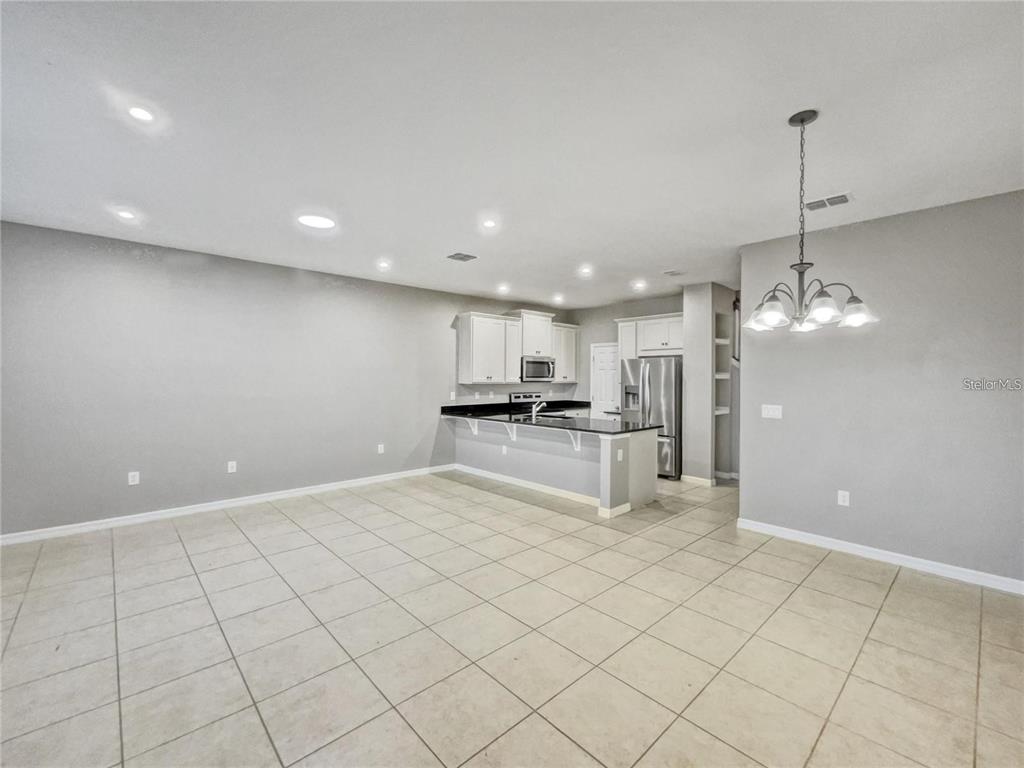 An open-concept kitchen features white cabinets, black countertops, and tile flooring — 2424 BLOWING BREEZE AVENUE, KISSIMMEE, FL