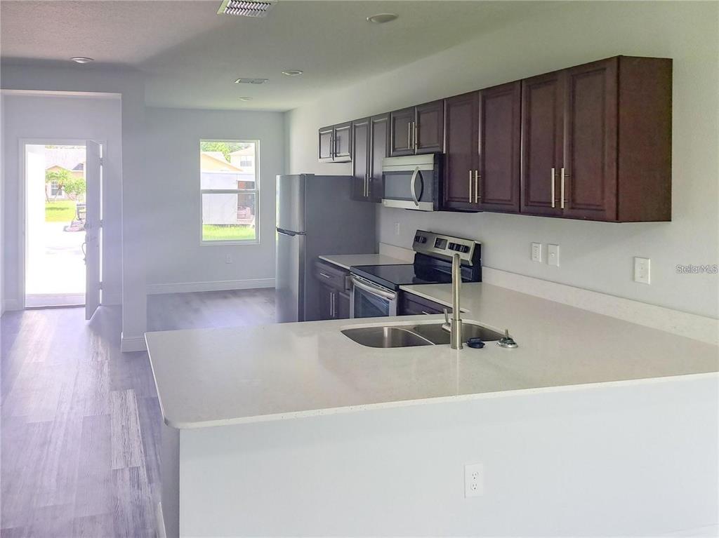 A kitchen features dark wood cabinets, stainless steel appliances, and a white quartz countertop island — 1030 NW 57TH COURT UNIT 1032, OCALA, FL