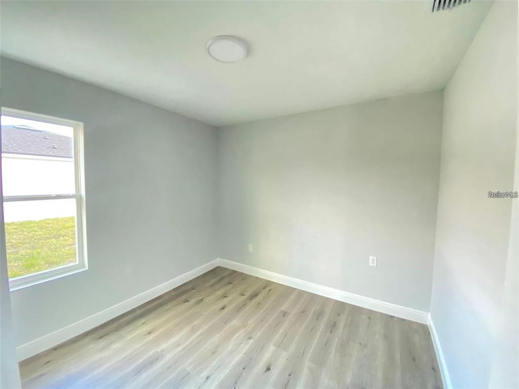 An empty bedroom features light gray walls, white trim, and wood-look vinyl plank flooring — 1030 NW 57TH COURT UNIT 1032, OCALA, FL