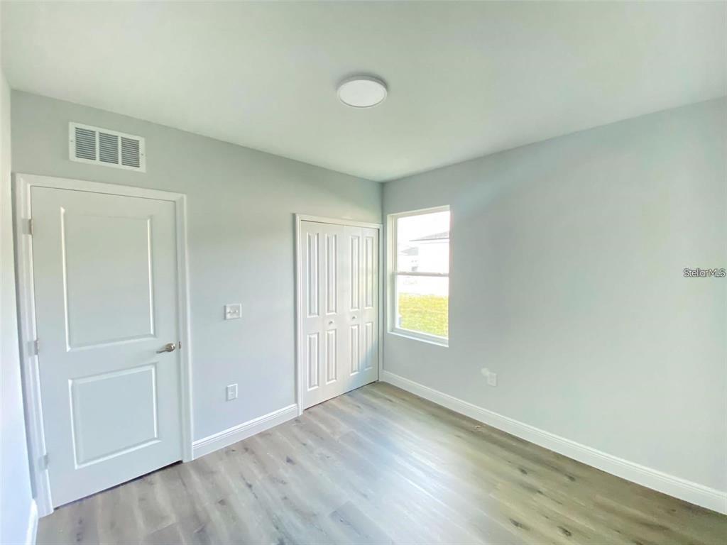 A bedroom with light gray walls, wood-look flooring, a closet, and a single window — 1030 NW 57TH COURT UNIT 1032, OCALA, FL