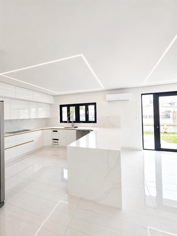 A modern white kitchen features a waterfall island, glossy cabinetry, and recessed linear ceiling lighting — Santa Teresita 2204 MCLEARY ST, SAN JUAN, PR