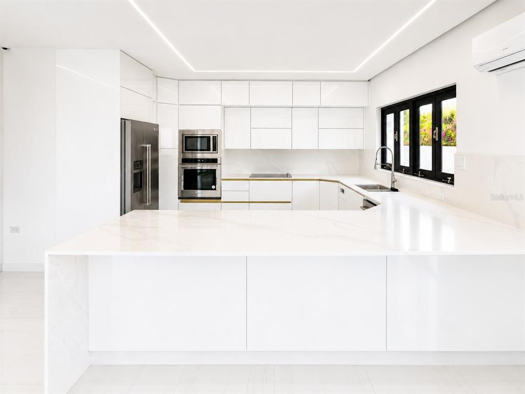 A modern white kitchen features a large peninsula, stainless steel appliances, and marble-look countertops — Santa Teresita 2204 MCLEARY ST, SAN JUAN, PR