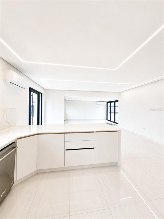 A modern, minimalist kitchen with white cabinetry and glossy tile flooring opens to a living area — Santa Teresita 2204 MCLEARY ST, SAN JUAN, PR