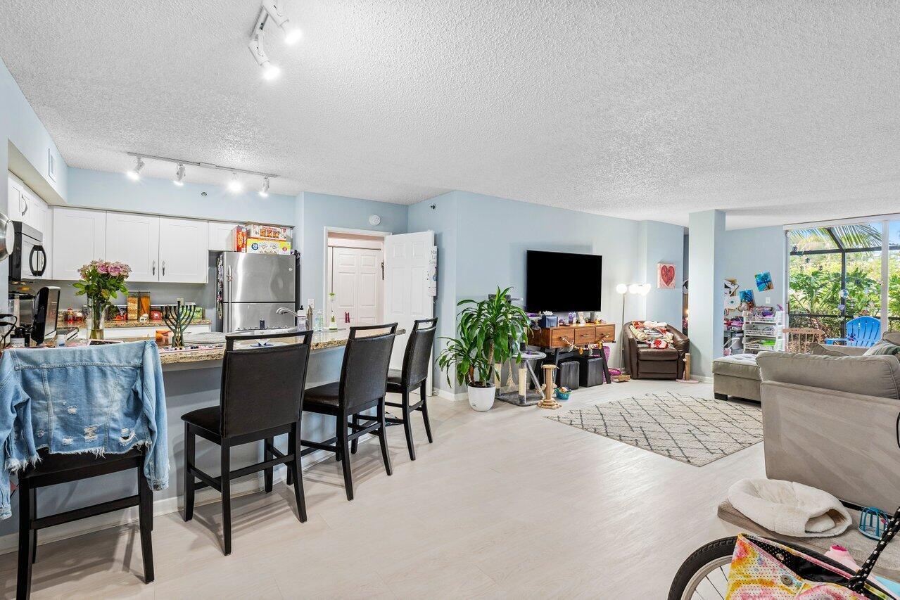 An open-concept living room and kitchen featuring light blue walls, tile flooring, and bar seating — 3111 Clint Moore Road, Boca Raton FL 33496, BOCA RATON, FL