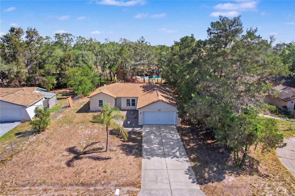 An aerial view shows a single-story house with a tan roof, garage, and palm tree — 6311 PINEHURST DRIVE, SPRING HILL, FL