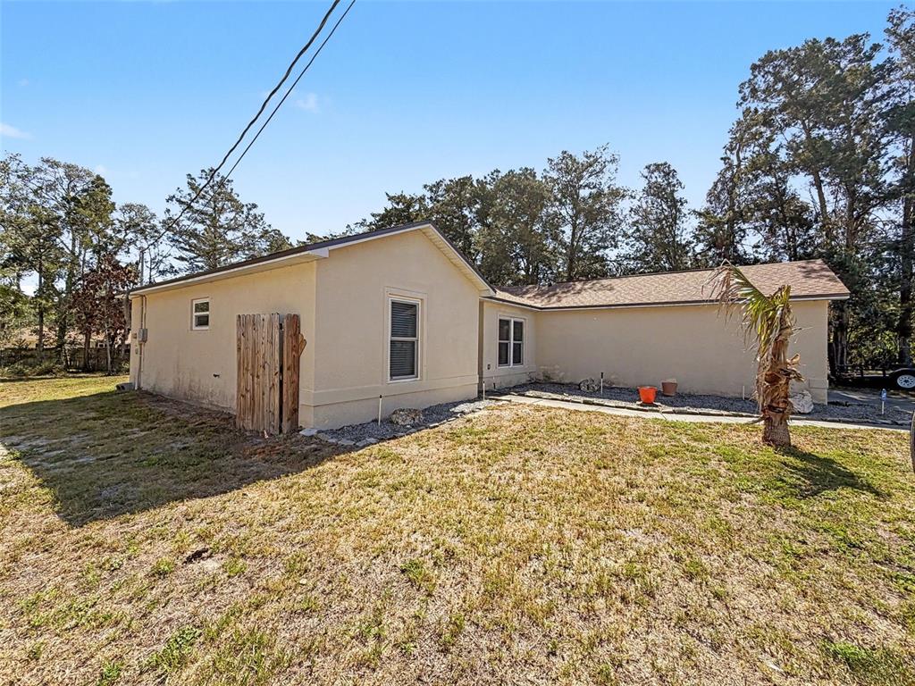 The exterior of a tan, single-story house features a wooden privacy screen and a palm tree — 6311 PINEHURST DRIVE, SPRING HILL, FL