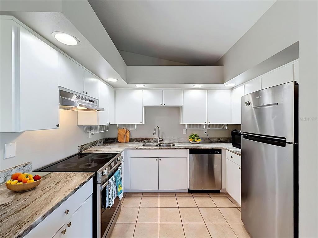 A kitchen features white cabinets, stainless steel appliances, granite countertops, and light-colored tile flooring — 6311 PINEHURST DRIVE, SPRING HILL, FL
