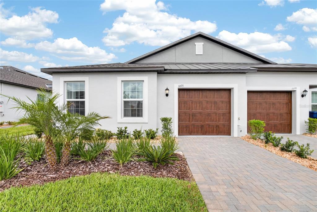 A single-story house exterior features a gray stucco facade, a brown garage door, and landscaping — 6693 HOMEBOUND WAY, NEW PORT RICHEY, FL
