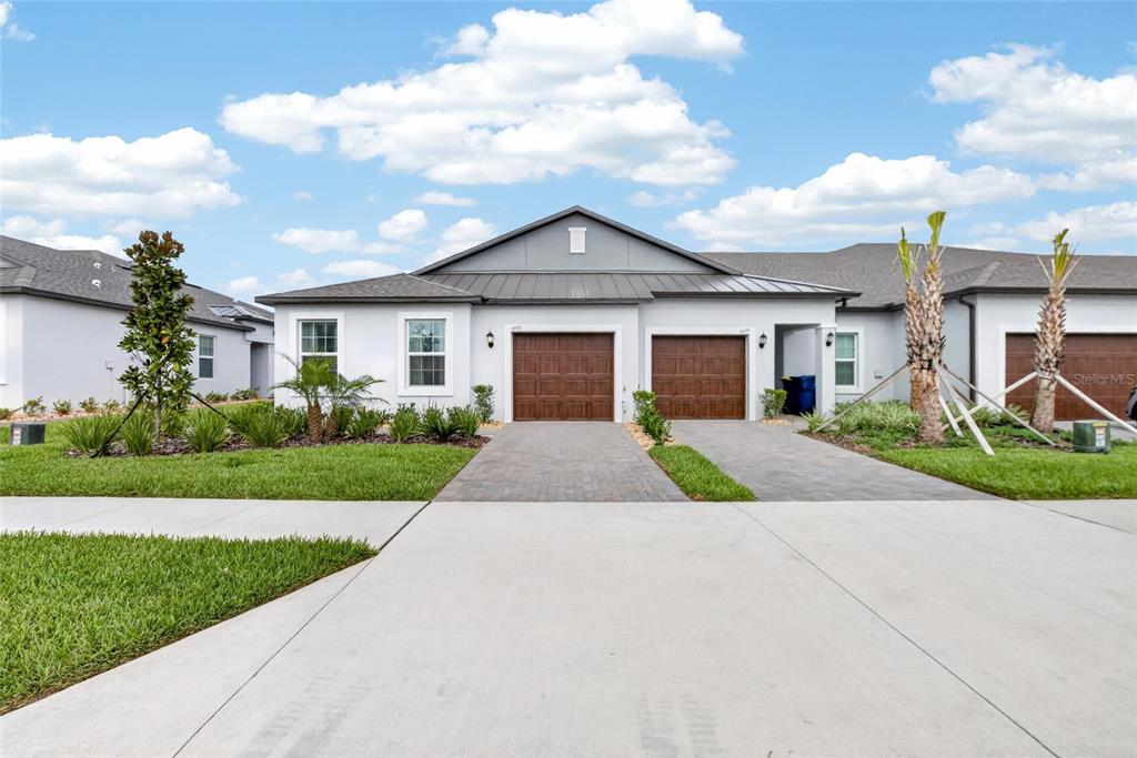 A single-story duplex with two brown garage doors, gray siding, and paved driveways — 6693 HOMEBOUND WAY, NEW PORT RICHEY, FL