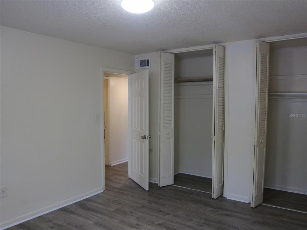 A bedroom features light-colored walls, wood-look flooring, and two open louvered-door closets — 300 NW 20TH AVENUE UNIT 6, GAINESVILLE, FL