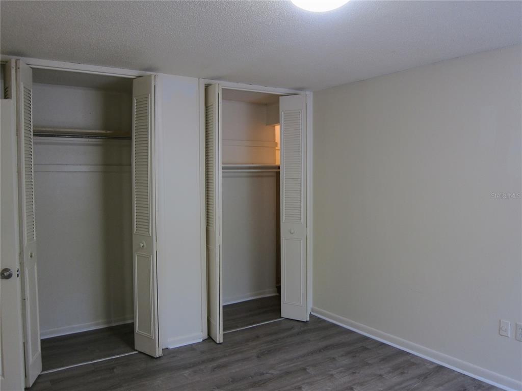 A bedroom features two open closets with louvered doors and gray wood-look flooring — 300 NW 20TH AVENUE UNIT 6, GAINESVILLE, FL
